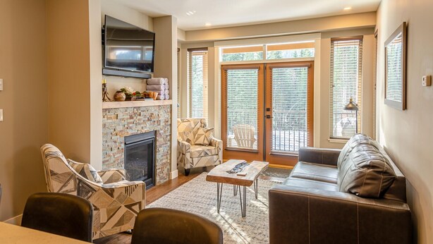 A living room with a fireplace, a flat-screen TV mounted above it, and a sofa. There are two chairs and a small table in the room.