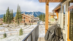 A mountain lodge with a balcony overlooking a snowy landscape and a ski slope.
