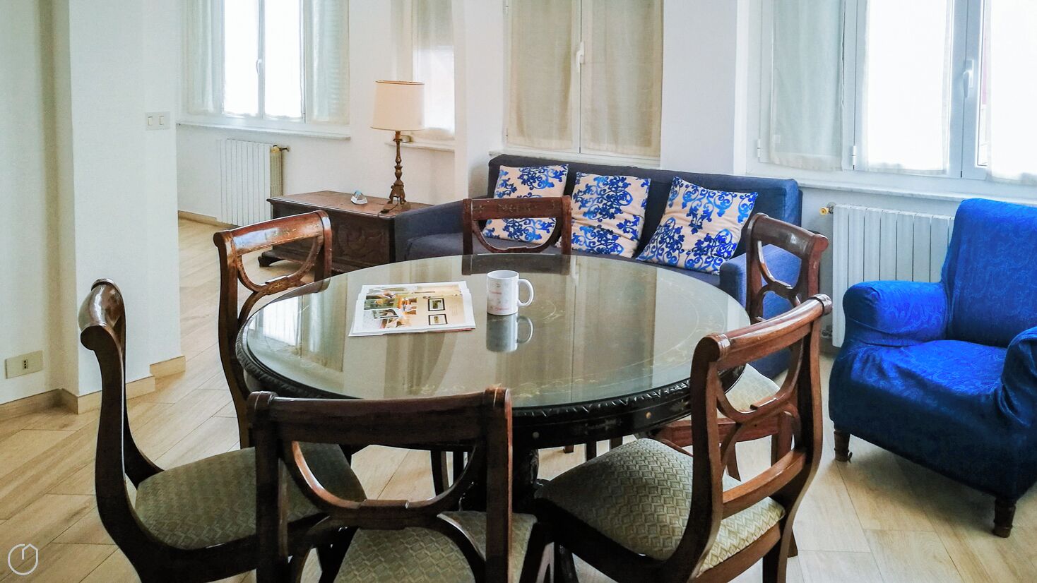Une table ronde en verre, entourée de chaises en bois, un canapé bleu et une lampe.