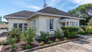 Une maison à deux étages, avec un toit recouvert de tuiles, des murs extérieurs blancs et un petit porche agrémenté de volets blancs.