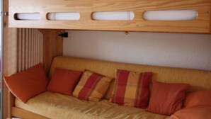 Ein Etagenbett mit Holz-Kopfteil und eine Schlafcouch mit orangefarbenen Kissen.