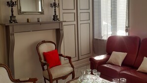 Een woonkamer met een open haard, een rode bank, twee fauteuils, een salontafel met glazen en een kaars, en een grote spiegel boven de open haard.