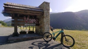 Ein Holzschild mit den Aufschriften "Vans" und "Bienvenue" kennzeichnet einen Empfangsbereich, davor ein Mountainbike und im Hintergrund eine Berglandschaft.