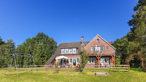 A two-story house with a balcony, a swing set, and a fenced yard. - Vacation home Koppelblick in the house Hohe Lucht in Dunum - Holiday home Koppelblick in the house Hohe Lucht in Dunum (Dunum)