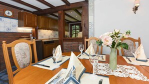A dining area with a wooden table set for a meal, a vase with flowers, and a brick wall with a clock. - Vacation home Koppelblick in the house Hohe Lucht in Dunum - Holiday home Koppelblick in the house Hohe Lucht in Dunum (Dunum)