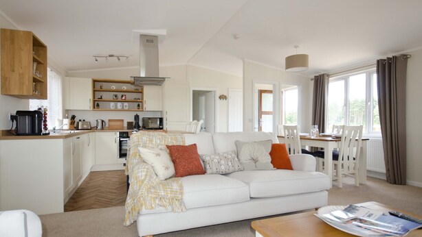 Een moderne, goed verlichte woonkamer met een witte bank, een houten salontafel en een keukenhoek met witte kasten en een inbouwmagnetron.