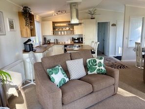 A living room with a brown sofa, a dining table, and a kitchen in the background. - Hollicarrs - Woodland Lodge (York)