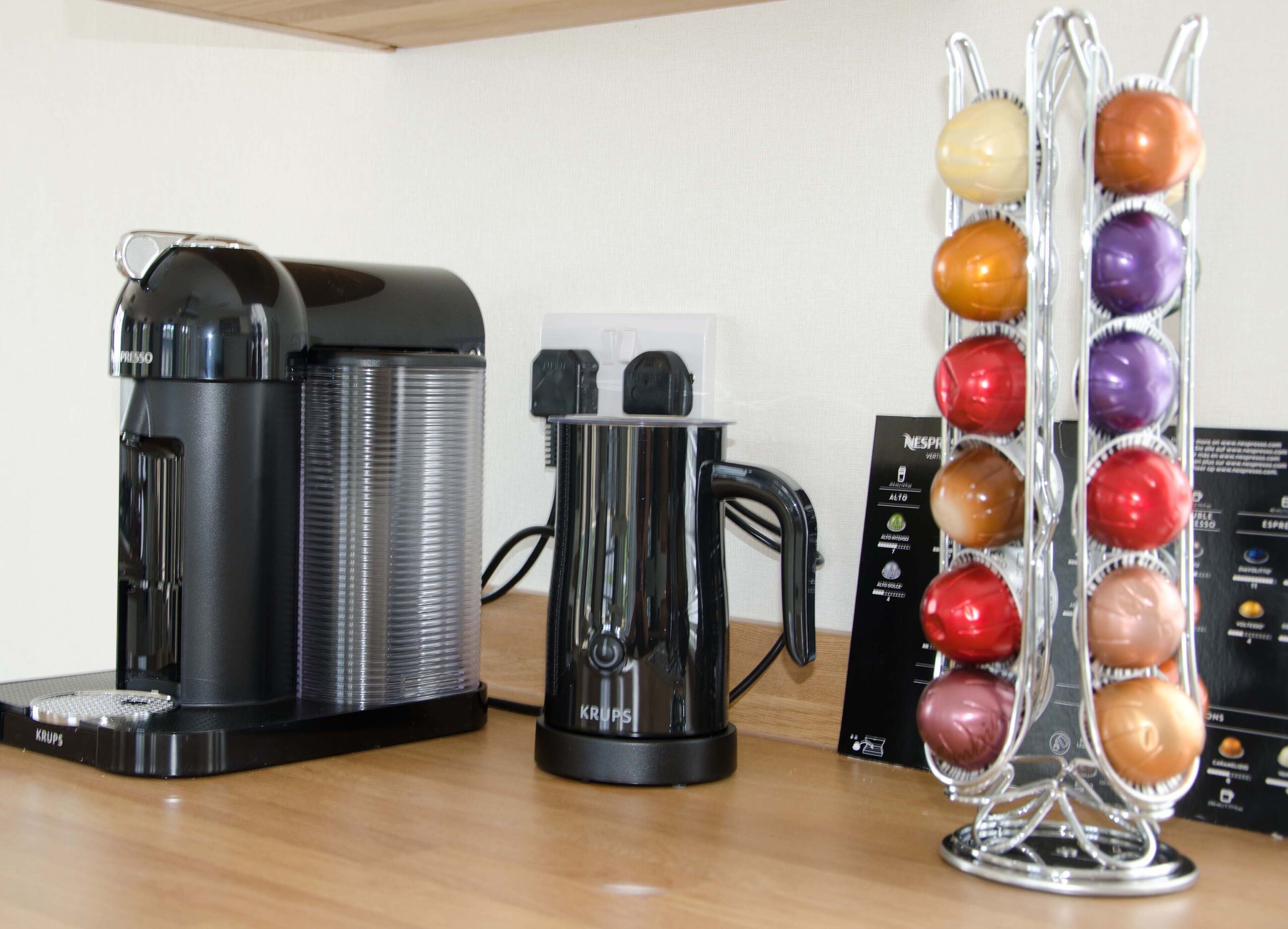 A coffee maker, a Krups coffee pot, and a coffee pod holder on a wooden surface.