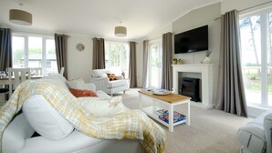 Een woonkamer met een witte bank, een salontafel, een open haard en een aan de muur bevestigde televisie.