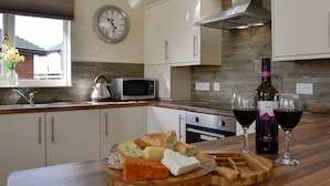 Una cocina moderna con armarios blancos, microondas, reloj y encimera de madera con queso, pan y copas de vino.