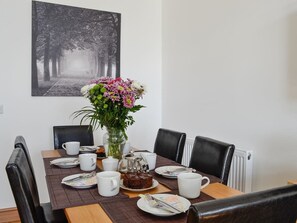 Una mesa de comedor preparada para dos, con un florero, un hervidor de agua y un plato de comida.