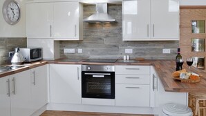 Una cocina moderna con armarios blancos, horno empotrado, microondas y encimera de madera.
