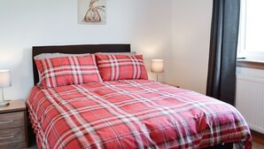 Una cama con colcha de cuadros rojos y blancos, cabecera de madera y dos lámparas de noche.
