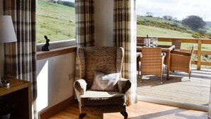 Una habitación acogedora con una ventana con cortinas a cuadros, un sillón mullido y un comedor con mobiliario de mimbre.