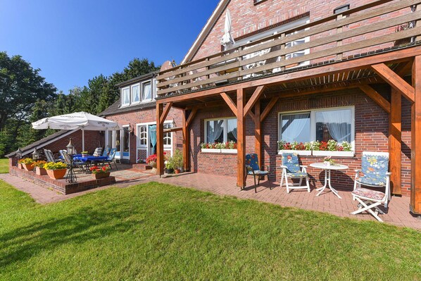 A brick house with a wooden deck, outdoor seating, and potted plants.