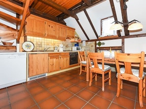 A rustic kitchen with wooden cabinets, a tiled backsplash, and a dining area with wooden chairs.