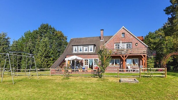 Een tweelaags huis met een terras, een schommel en een tuin.