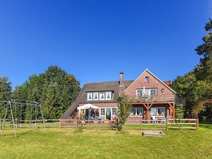 A two-story house with a patio, a swing set, and a garden.