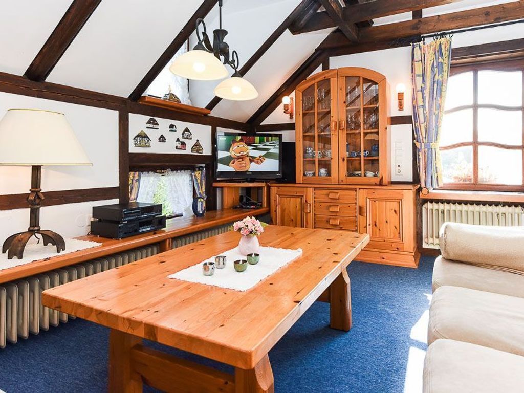 Una habitación acogedora con una mesa de madera, un sofá, un aparador con puertas de cristal, un televisor y una ventana con cortinas.
