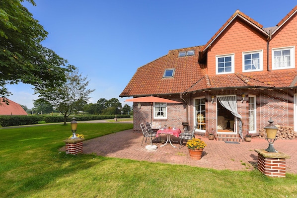 A brick house with a patio, outdoor seating, and a well-maintained lawn.