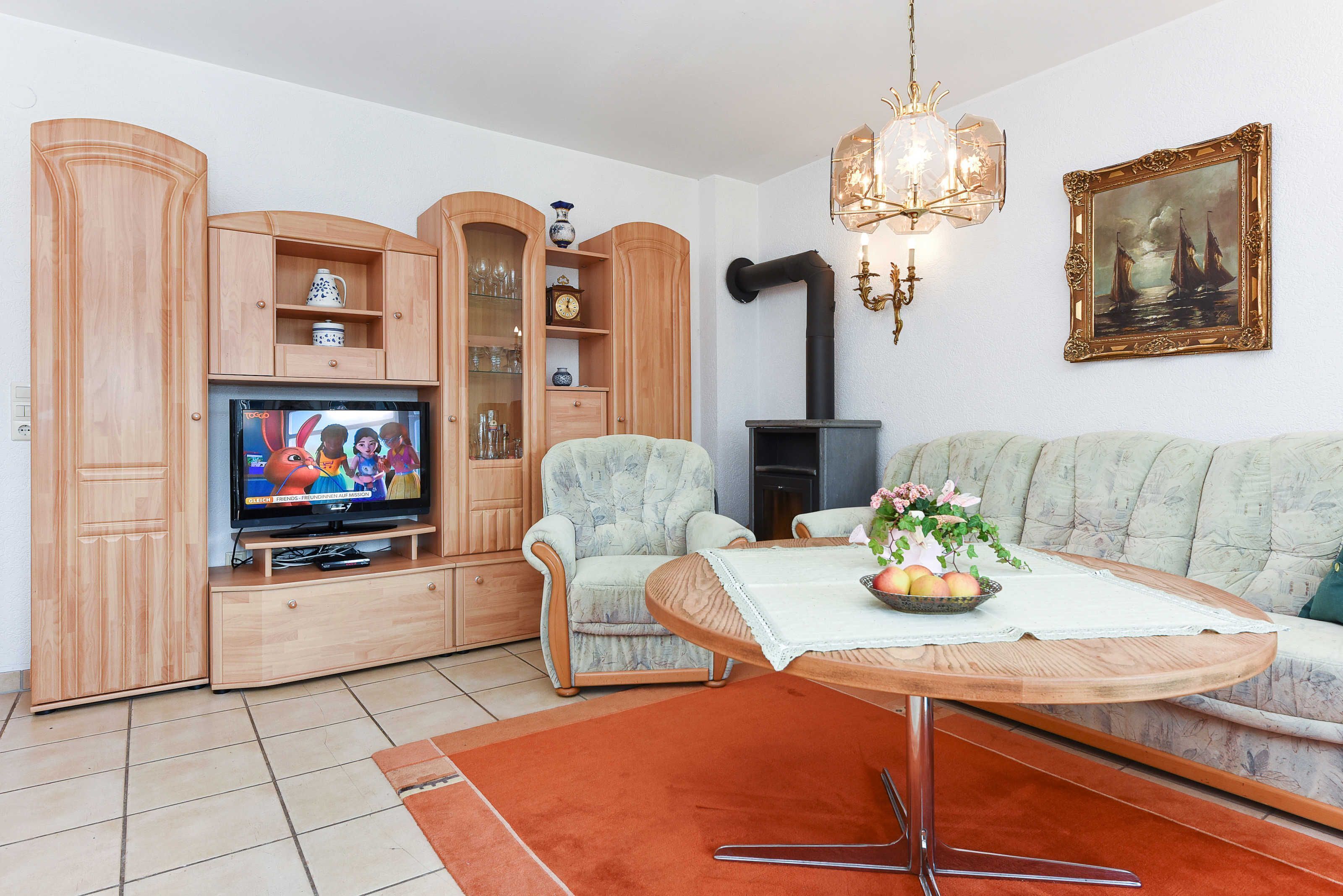 A living room with a television, wooden cabinets, a sofa, a table with a vase, and a fireplace.