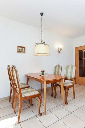 A dining area with a wooden table and chairs, a hanging lamp, a wall-mounted light fixture, and a door with glass panels.