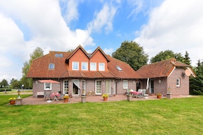 A two-story brick house with a red-tiled roof, a covered patio with outdoor furniture, and a well-maintained lawn.