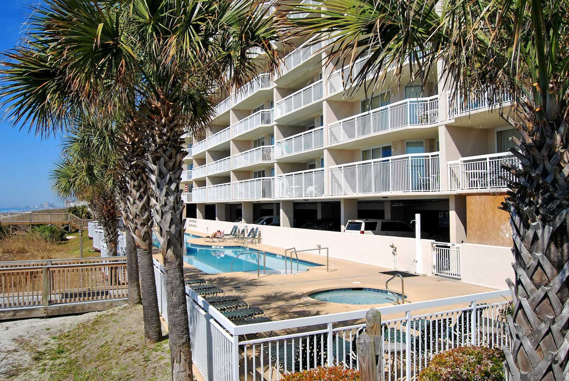 A multi-story hotel with balconies, a swimming pool, and palm trees.