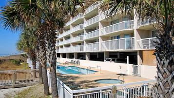 A multi-story hotel with balconies, a swimming pool, and palm trees.