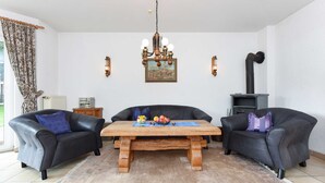 Een woonkamer met een houten tafel, twee zwarte leren banken, een kroonluchter, een schilderij en een open haard.