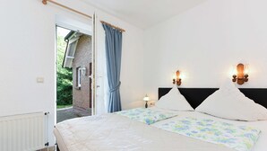 Een slaapkamer met een bed, twee wandlampen, een raam met gordijnen en een radiator.