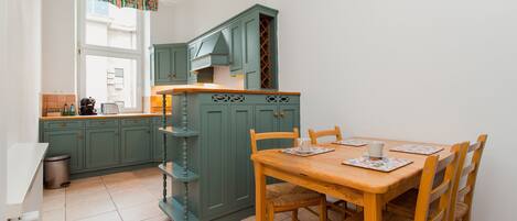 A kitchen with teal cabinets, a wooden dining table, and a window with a curtain.