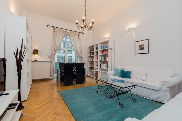 Ein modernes Wohnzimmer mit einem weißen Sofa, einem türkisfarbenen Teppich, einem schwarzen Metall-Couchtisch und einem Bücherregal.