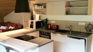 Eine moderne Küche mit einer zentralen Kochinsel, einem eingebauten Backofen und einem Spülbecken. Es gibt Barhocker und eine Pendelleuchte über der Insel.