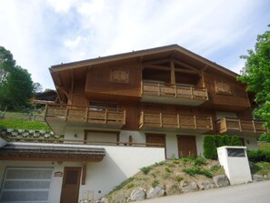 A two-story wooden chalet with balconies, a garage, and a stone wall.