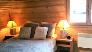 Ein gemütliches Schlafzimmer im Blockhausstil mit einem Bett, zwei Nachttischen mit Lampen, einem Heizgerät und einem Fenster.