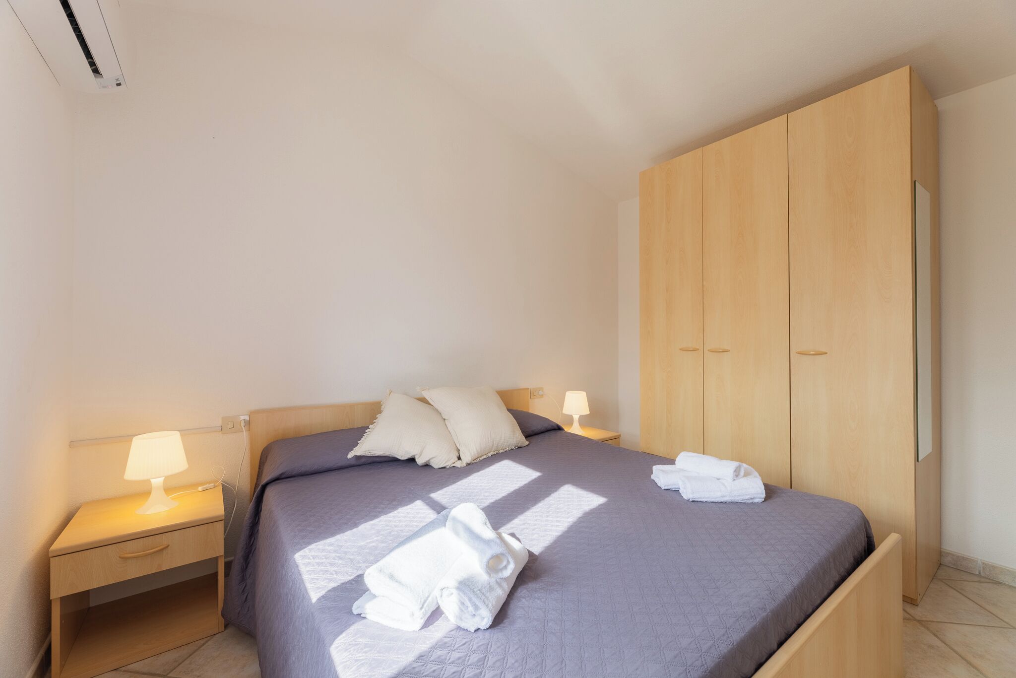 A neatly made bed with pillows, a bedside lamp, and a folded towel on the bed.