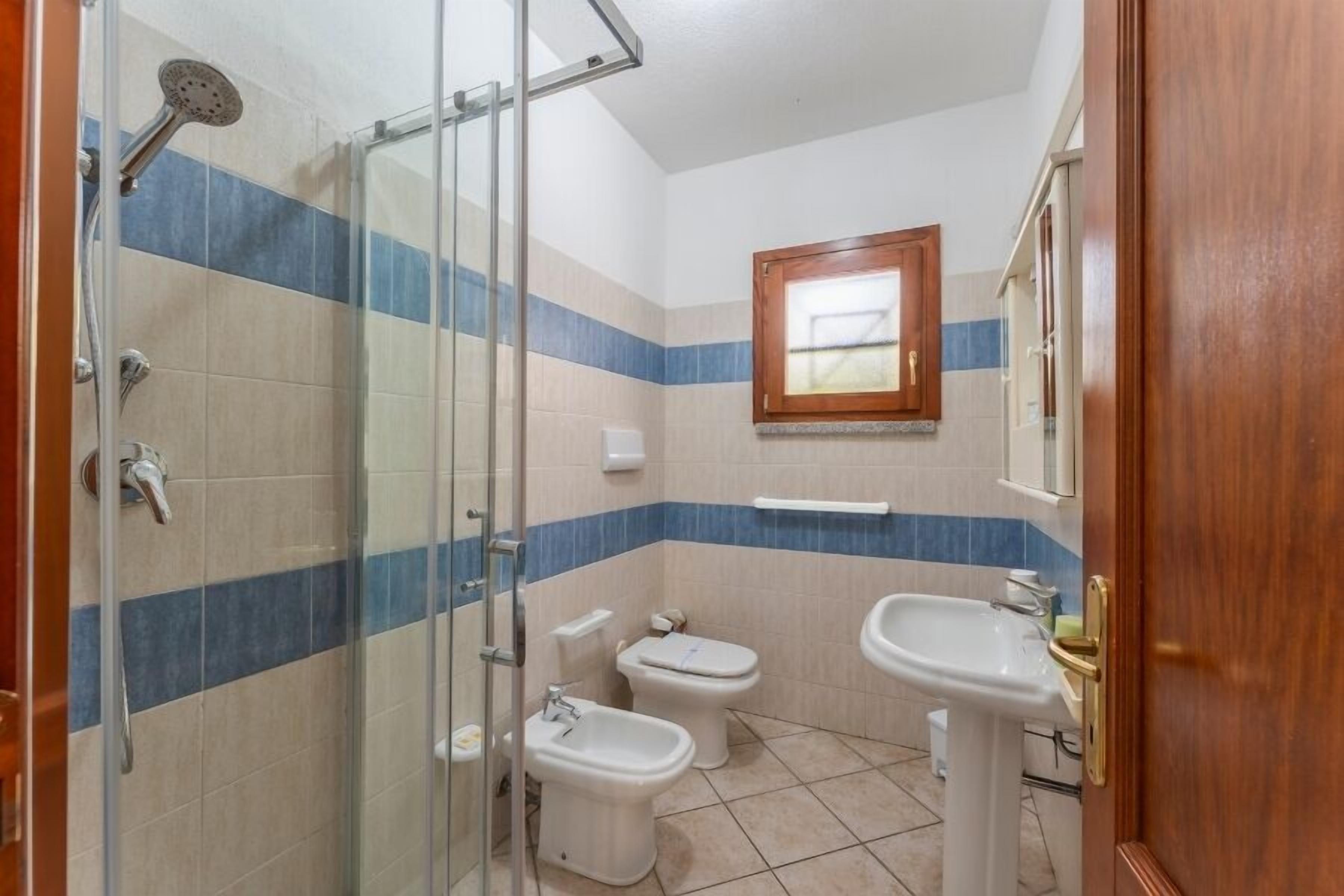 A bathroom with a glass shower enclosure, two toilets, a bidet, and two sinks.
