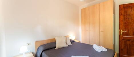Quarto com cama, mesa de cabeceira, luminária e guarda-roupa de madeira.