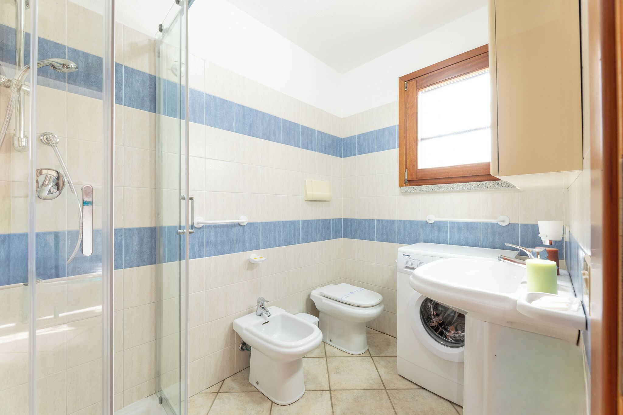 A bathroom with a glass shower enclosure, a bidet, a toilet, and a washing machine.