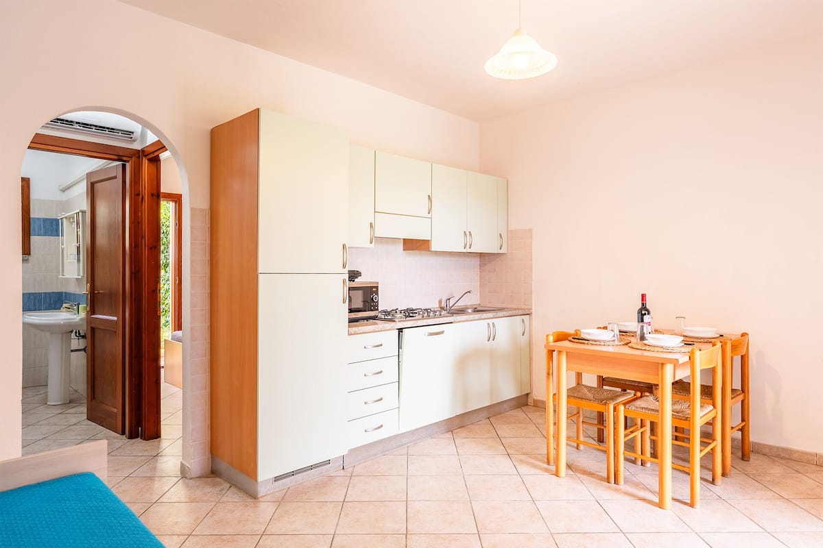 Una cocina compacta con armarios blancos, una mesa de comedor con sillas y un lavamanos visible.