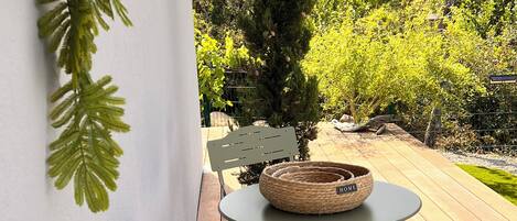 A patio with a round table and two chairs, a woven basket on the table, and a tall conifer tree in the background.