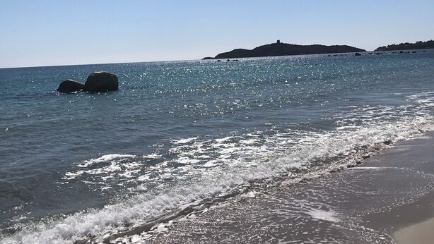 Une plage avec une eau cristalline, des vagues et une île qui se dessine à l’horizon.