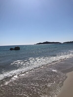 Una spiaggia con acqua cristallina, onde e un'isola in lontananza.