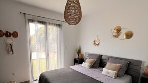 Une chambre à coucher moderne, dotée d’un grand lit, d’un luminaire suspendu en fibres tressées et offrant une vue sur l’extérieur grâce à une grande fenêtre.