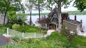 A lakeside cottage with a porch, a deck, and a fenced yard.