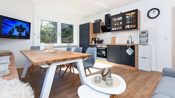Une cuisine moderne avec un coin repas, un téléviseur et une horloge au mur.