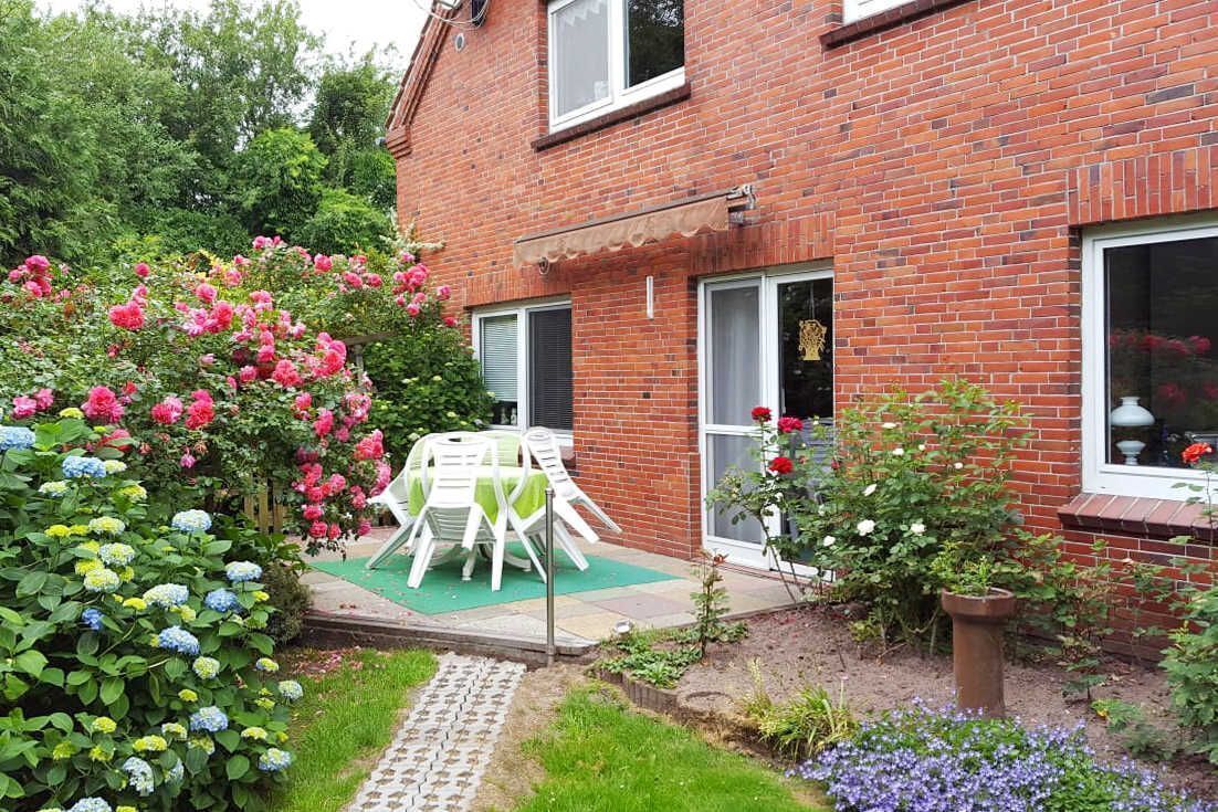 Ein Ziegelhaus mit Garten-Terrasse, einem Tisch mit Stühlen und verschiedenen blühenden Pflanzen.