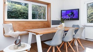Un espace repas moderne avec une table en bois, des chaises grises et un téléviseur fixé au mur.