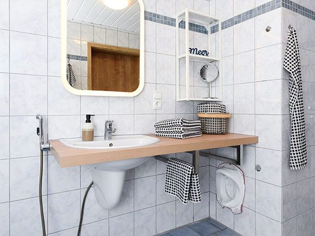 A bathroom with a sink, mirror, towel rack, and a shelf with folded towels.